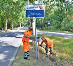 Norbert Borde (l.) und Mario Stöcker stellten in der vergangenen Woche an der B107 bei Glöwen das neue Begrüßungsschild auf. Foto: Bernd Atzenroth / Landkreis Prignitz
